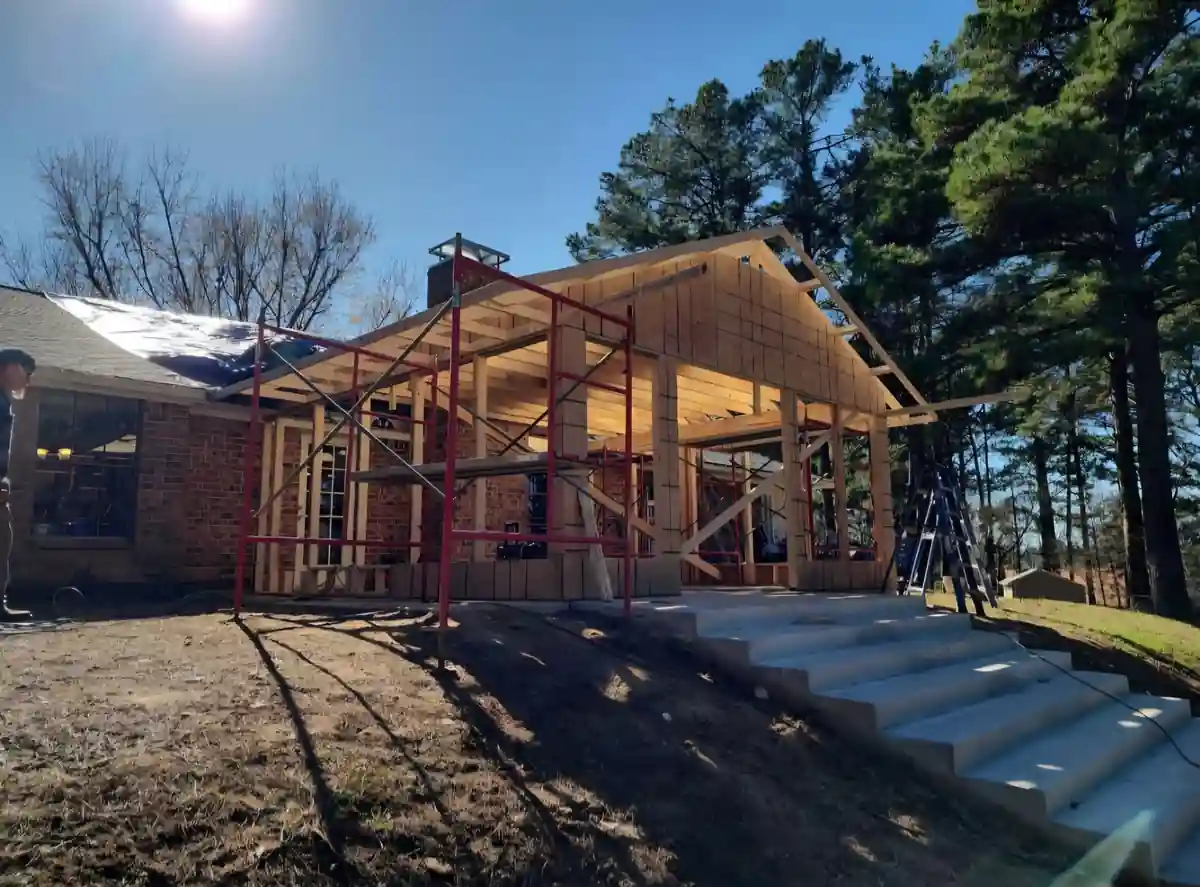 A room addition framed in timber against a brick ranch house, with red scaffolding and new concrete steps