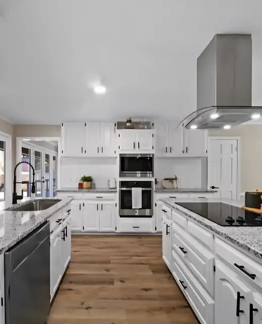 White kitchen with a stainless hood, built-in ovens and wood-look floor