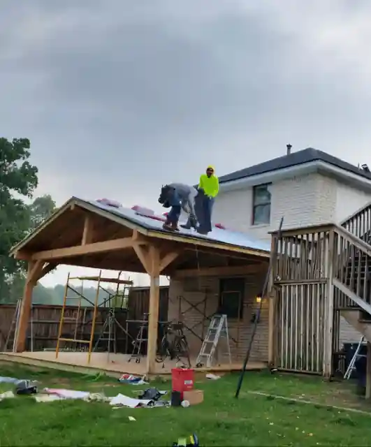 Crew roofing a new pavilion on a brick two-story house