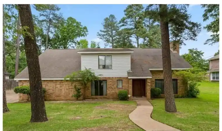 Tan brick two-story house under tall pines before painting
