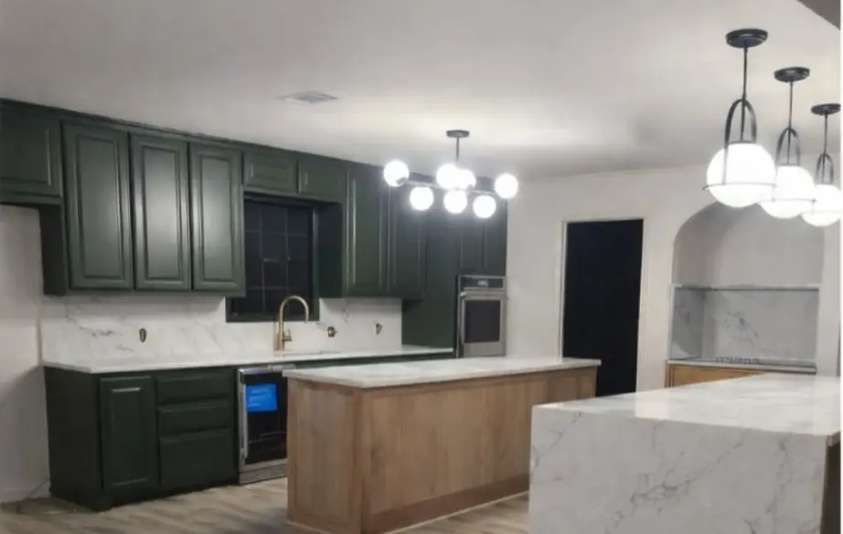 The same kitchen after: forest-green cabinets, a marble-look backsplash, a wood island, a waterfall counter and globe pendants