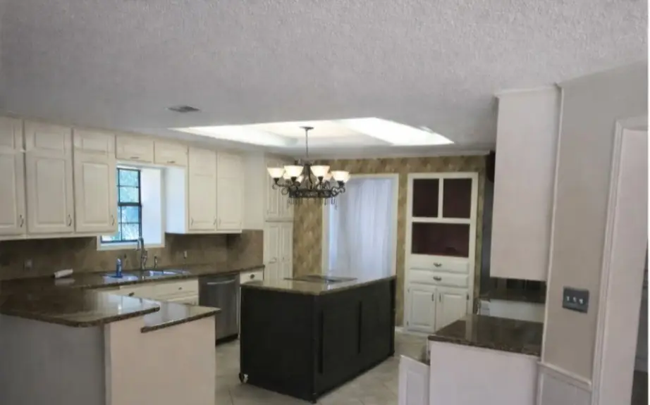 The kitchen before: cream cabinets, brown granite counters, a dark island and a fluorescent skylight box